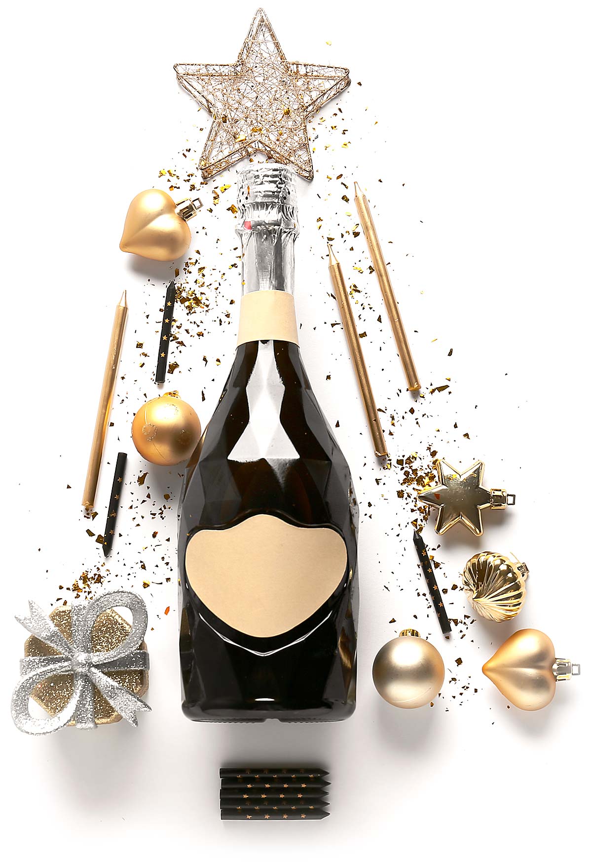 Black faceted champagne bottle surrounded by gold and black candles, gold Christmas ornaments, silver glittery gift box, and gold star decoration on white background.